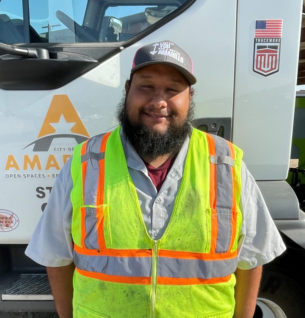 City of Amarillo street crew member Emilio Aguilera smiling in front of a street department vehicle, wearing a high-visibility vest and Amarillo-branded cap.
