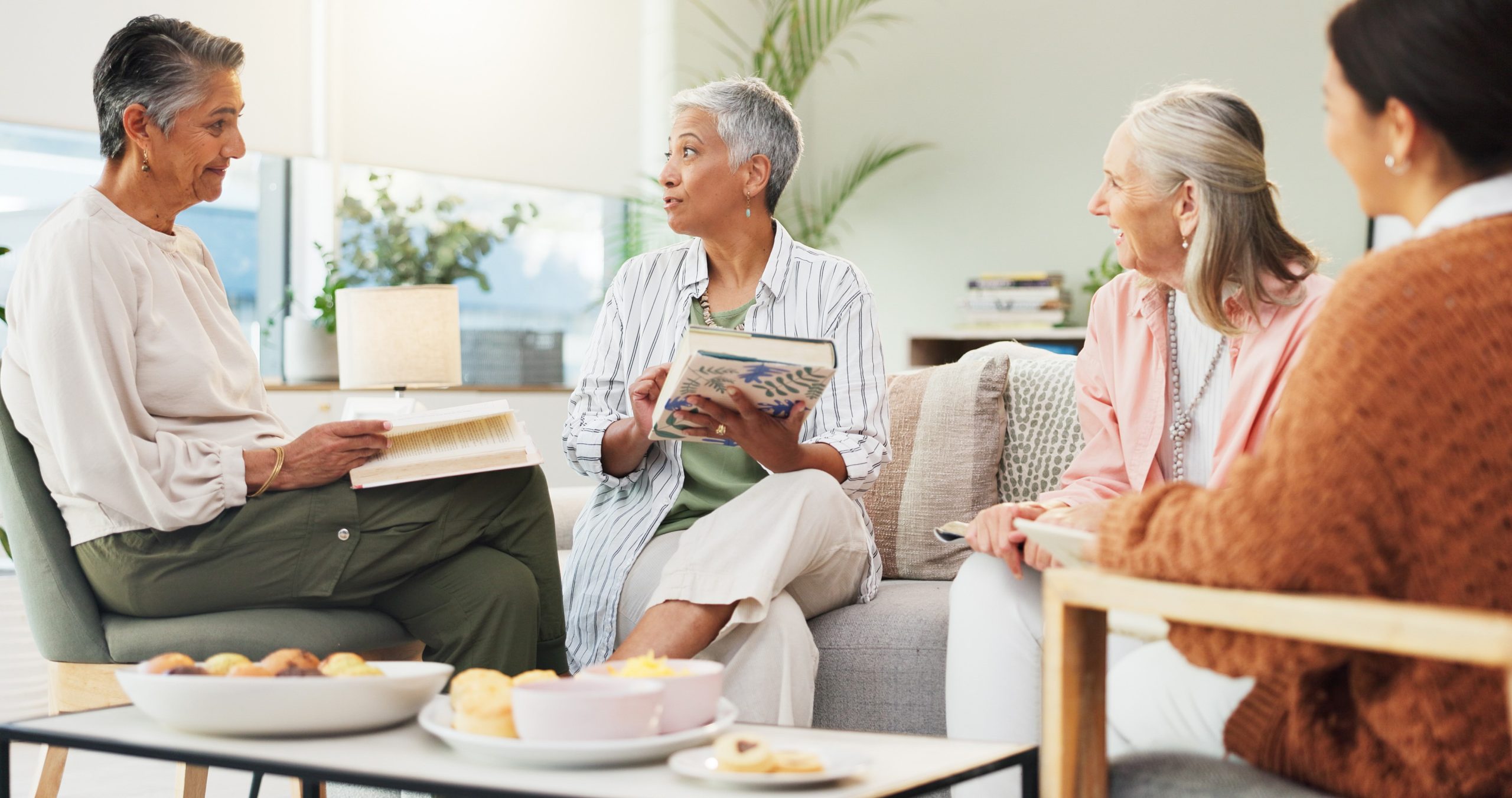A group of four older women sitting around a coffee table discussing a book