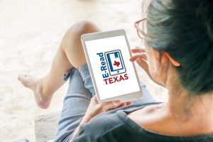 The back of a woman's head as she looks down at her iPad with the E-Read Texas logo on screen