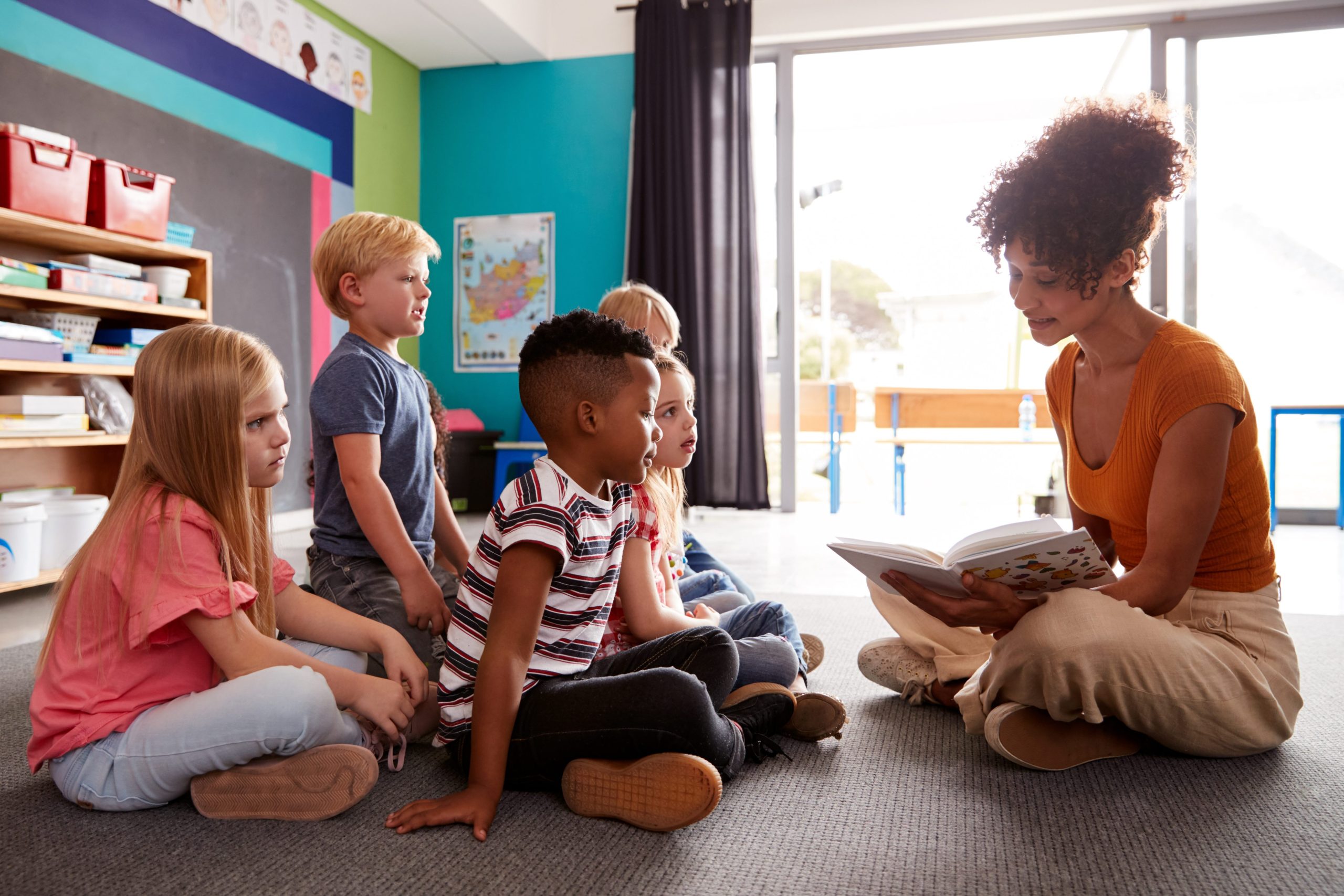 A woman reading a book to a group of children sitting on the group