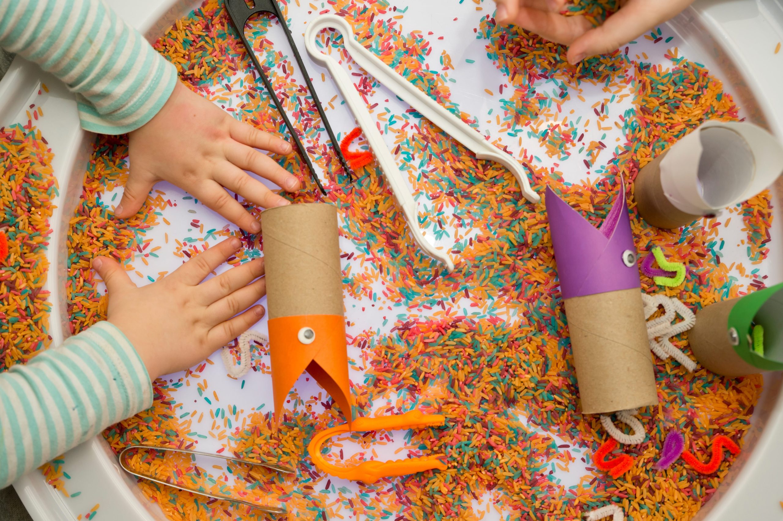An overhead shot of kids playing with colorful rice and other sensory tools