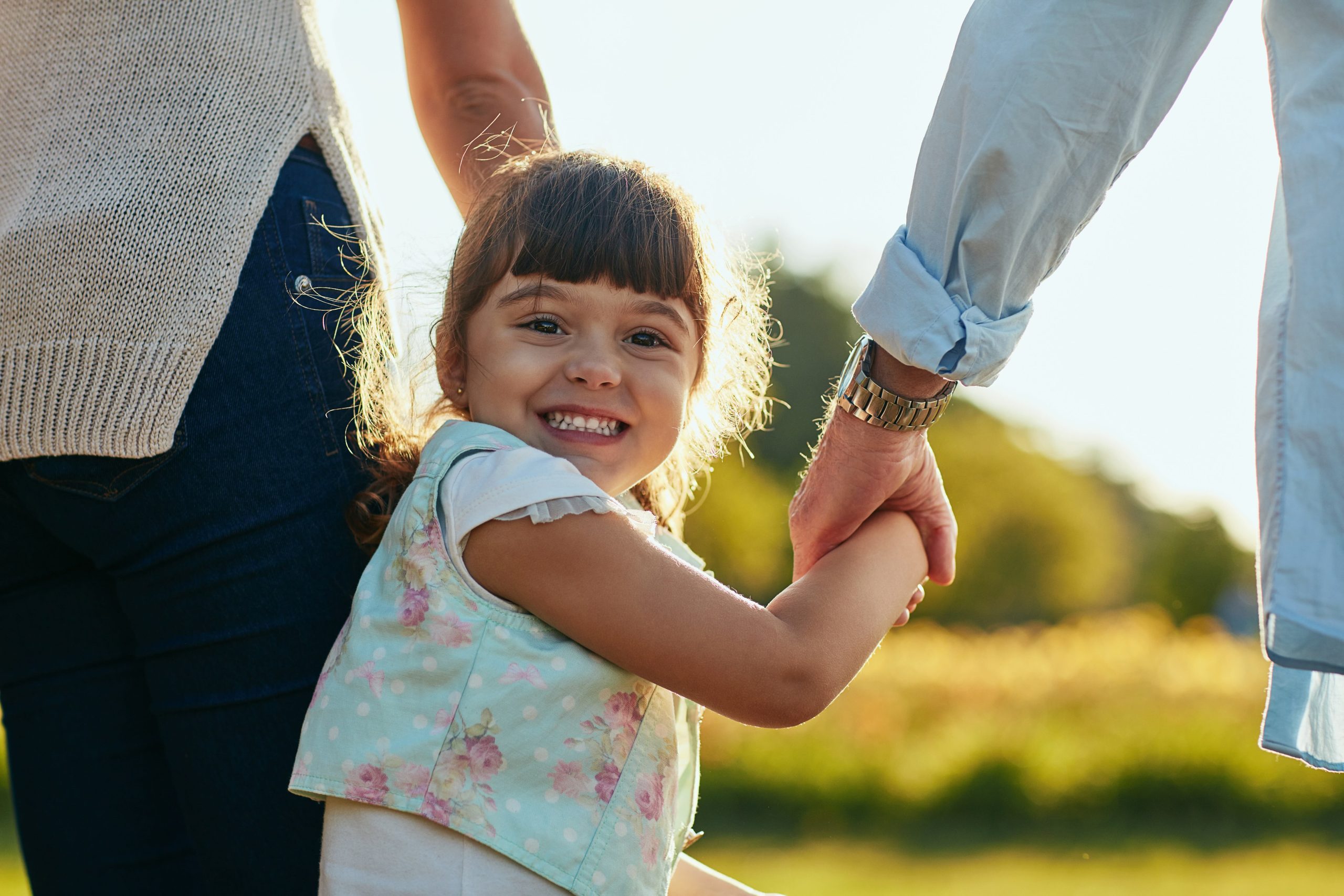 A young girl walking hand-in-hand with her parents outdoors