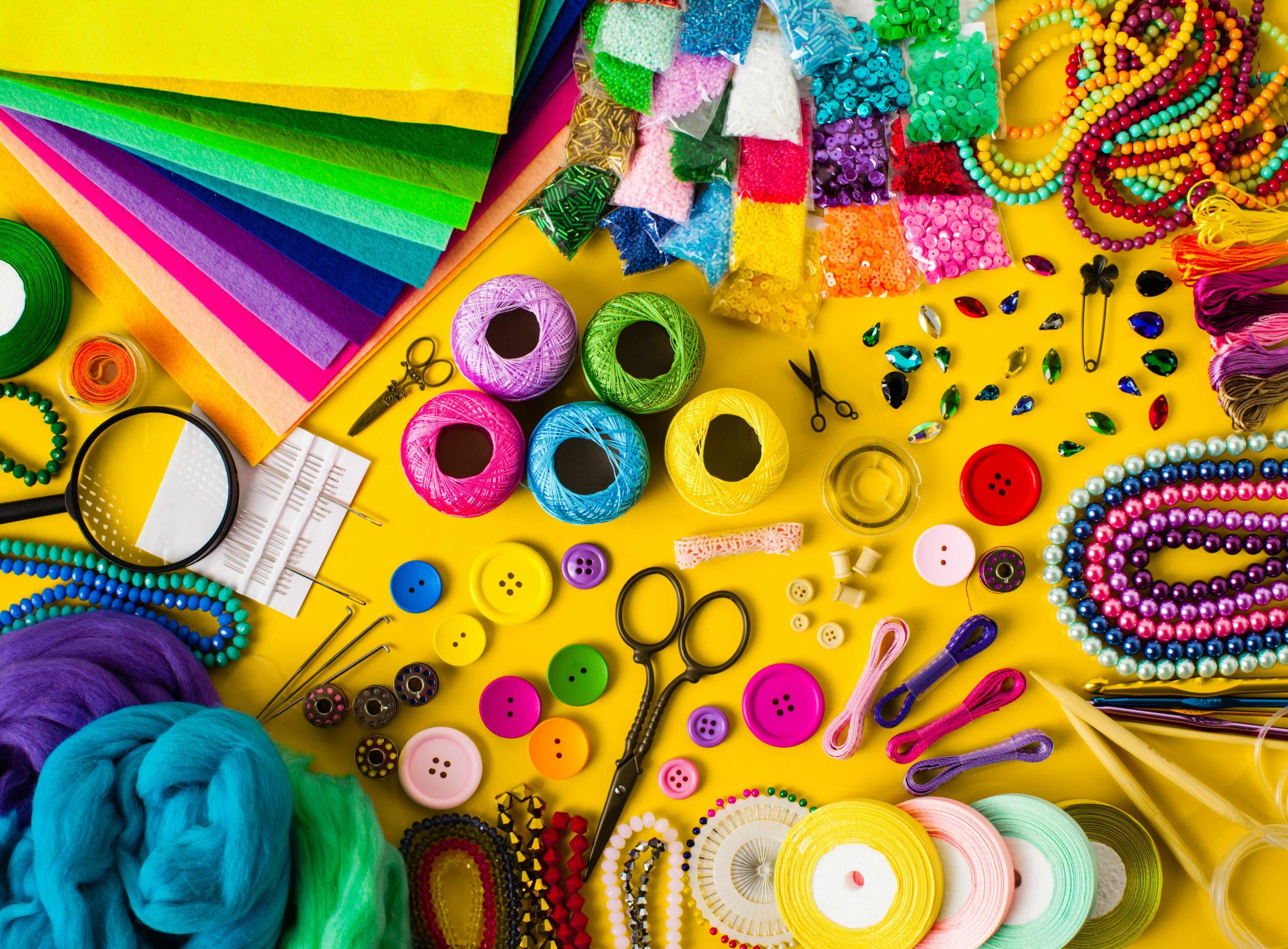 A variety of colorful craft supplies including yarn, felt paper, buttons, glitter, and thread