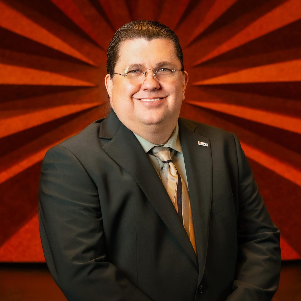Headshot of Civic Center's General Manager Christopher Post wearing glasses, a black blazer, and a yellow striped tie