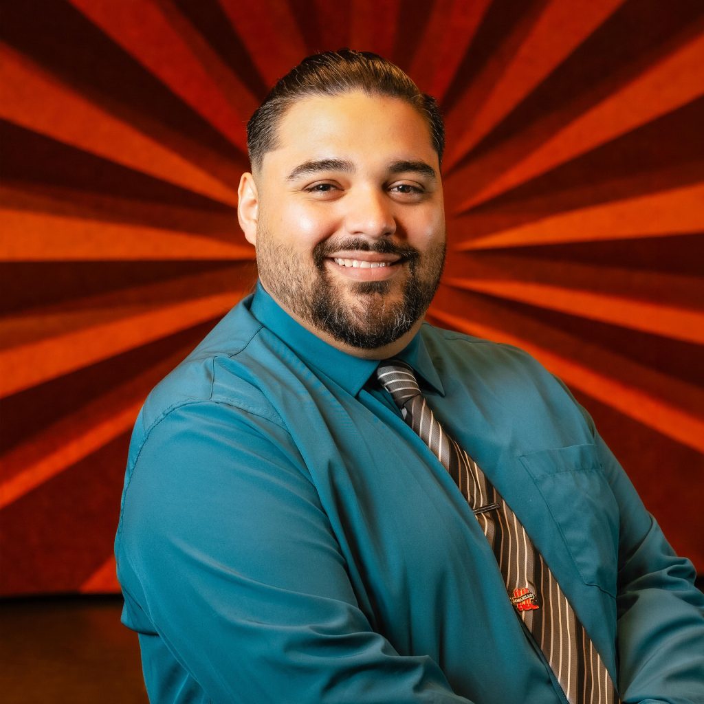 Headshot of Civic Center's Event Supervisor Josia Castro wearing a blue long sleeve button down and grey striped tie