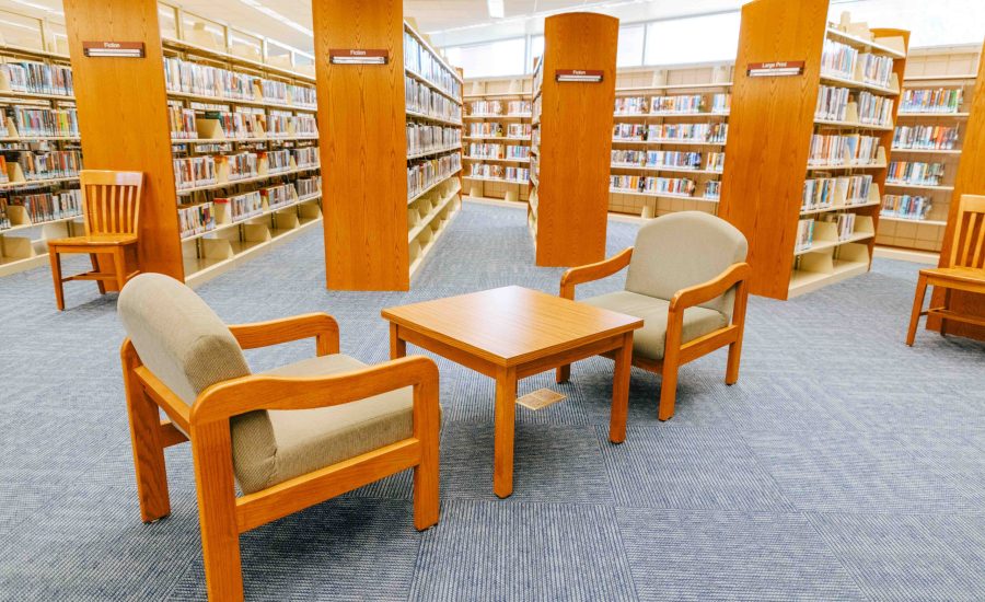 Rows of bookshelves with a seating area in the center featuring two chairs and a square table in the middle